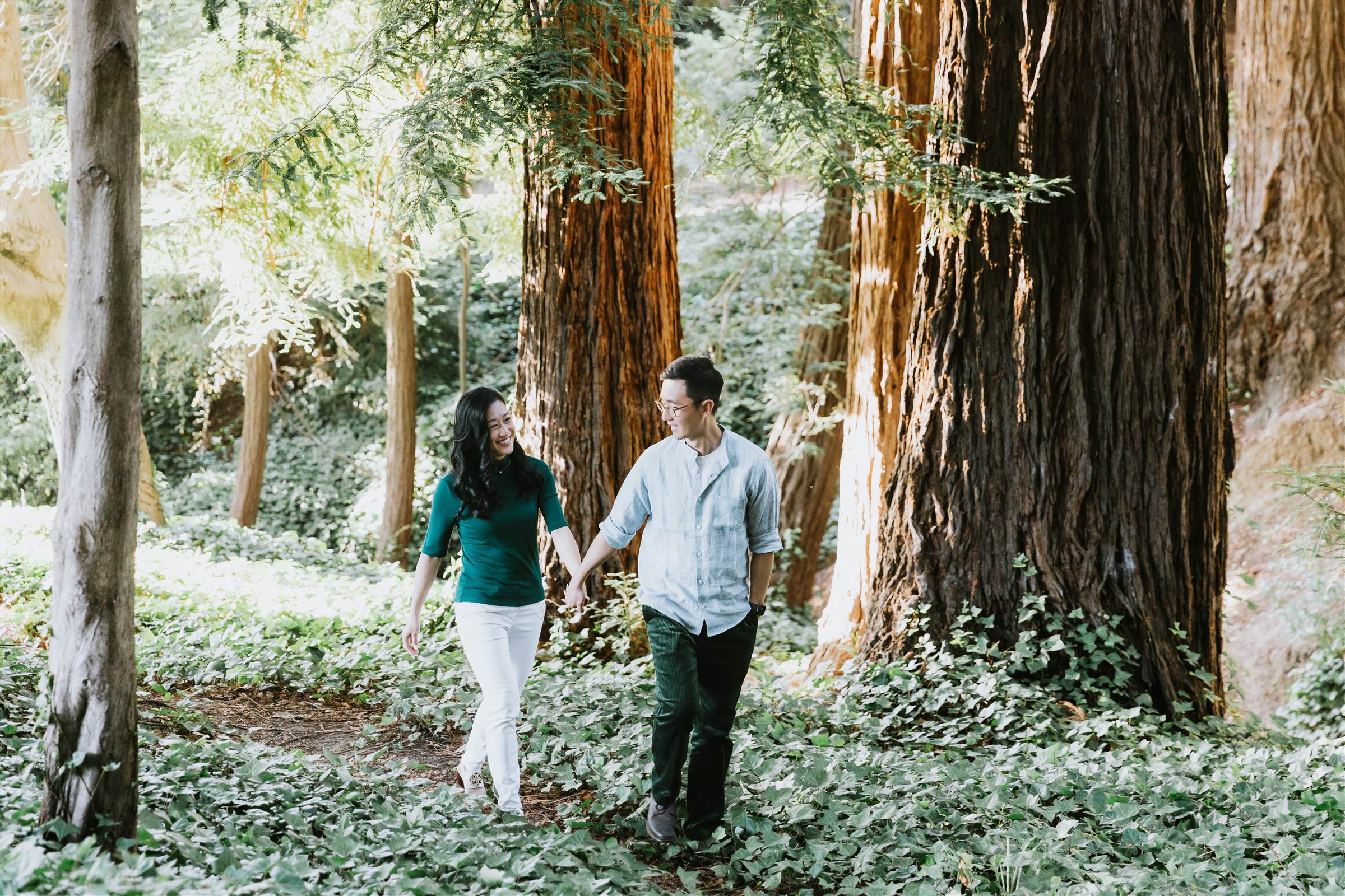 Helen and Richard walking hand in hand through a redwood grove