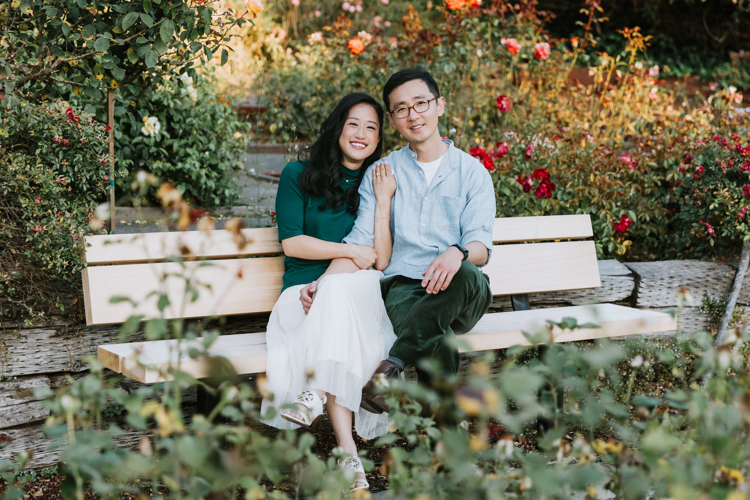 Helen and Richard sitting close on a bench in a rose garden in golden evening light